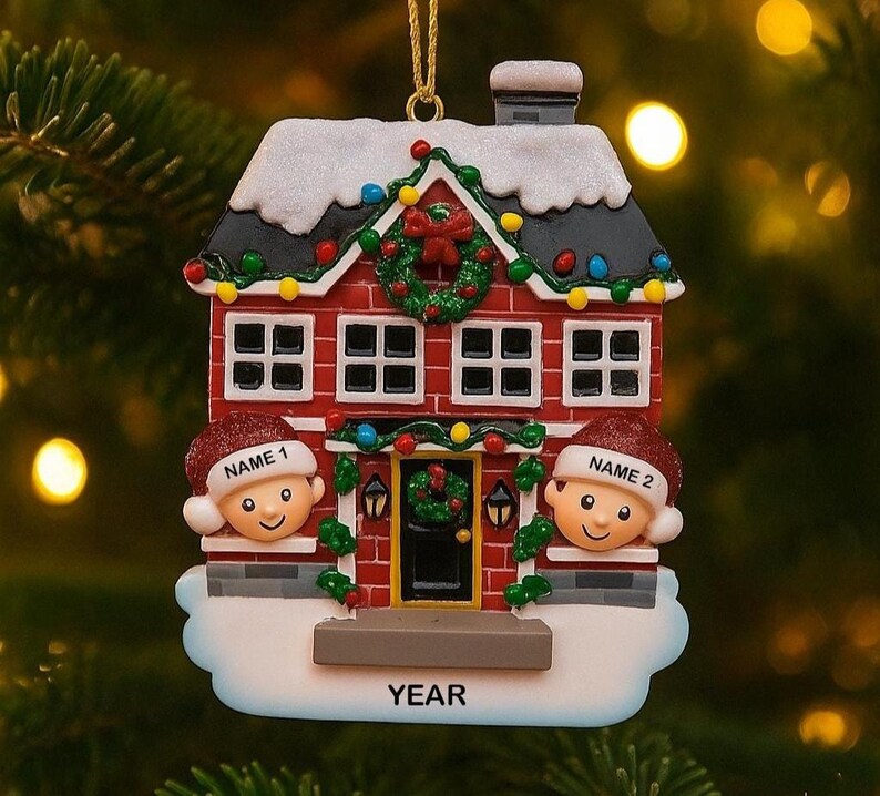 May include: A red and white Christmas house ornament with two smiling faces wearing Santa hats. The house has a wreath on the door and is decorated with lights and snow. The word "YEAR" is at the bottom.