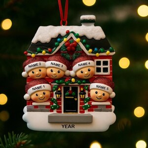 May include: A personalized Christmas ornament shaped like a house, featuring five smiling faces wearing Santa hats. The house is red with white snow accents, a black roof, and a small window. Each hat has a name on it. The word "YEAR" is at the bottom.