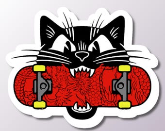 Peut inclure: Un chat noir à l'expression féroce mord un skateboard rouge avec un motif de dragon. Le skateboard a des trucks noirs et des roues jaunes.