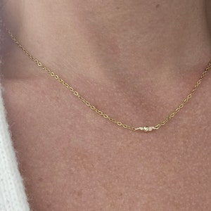 Op de afbeelding: Een delicate gouden ketting met een klein hartje en twee kleine kralen.