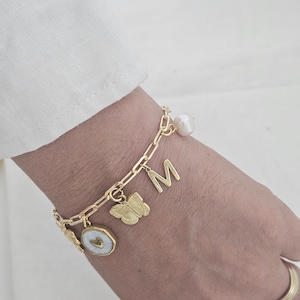 May include: Gold charm bracelet with a pearl, butterfly, heart, and letter M charm.
