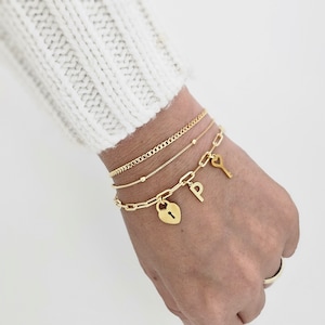 May include: Gold chain bracelet with a heart-shaped padlock charm, a key charm, and a letter "P" charm.