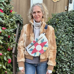 Peut inclure: Veste bomber en fausse fourrure beige avec col et poignets côtelés marron clair. Le jean bleu et les bottines noires complètent la tenue. Un sac banane blanc et à motifs avec un motif d'étoile est porté en bandoulière.