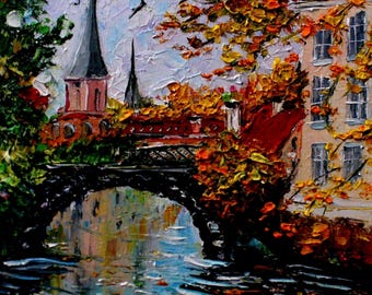 May include: An oil painting shows a European townscape with a bridge over a canal. The scene includes a church with spires, buildings with red roofs, and trees with autumn leaves. Birds are in the sky, and the water reflects the buildings and the sky.