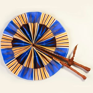 K&ouml;nnte beinhalten: Ein blauer und gelber F&auml;cher mit einem braunen Holzgriff. Der F&auml;cher ist aus Stoff mit einem geometrischen Muster.