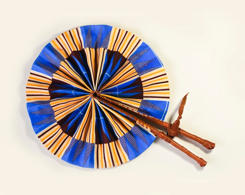 K&ouml;nnte beinhalten: Ein blauer und gelber F&auml;cher mit einem braunen Holzgriff. Der F&auml;cher ist aus Stoff mit einem geometrischen Muster.