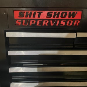 May include: Black metal toolbox with a red label that reads "Shit Show Supervisor".