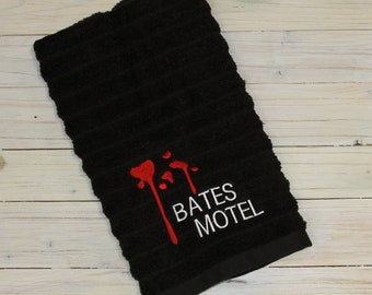May include: Black kitchen towel with red blood splatter and white embroidery that reads "Bates Motel".