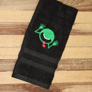 Peut inclure: Serviette de toilette noire avec un visage d'extraterrestre vert avec une langue rouge qui sort brodé dessus.