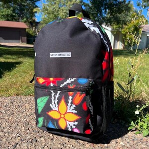 May include: Black backpack with a colorful floral design on the front pocket and side. The backpack has a black handle and a side pocket. The text "NATIVE IMPACT CO" is printed on the front.