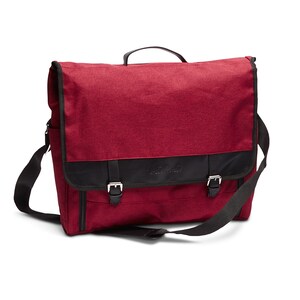 May include: A burgundy messenger bag with black straps and buckles. The bag has a black leather flap with the word "Nomad" embossed on it.