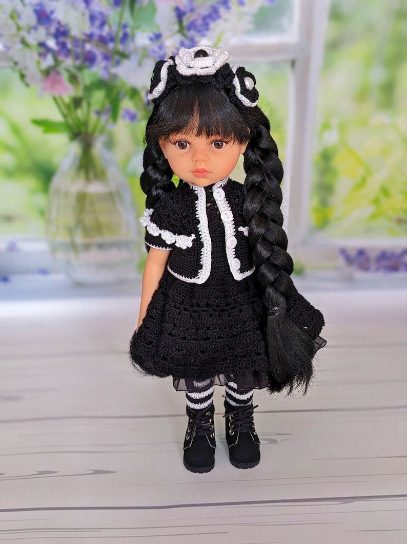 May include: A black and white crocheted dress with a white crocheted collar and a white crocheted headband. The doll has black hair and brown eyes.