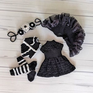 May include: A black crocheted dress, jacket, and leg warmers with white accents. A black and white crocheted headband with white flowers is also included.