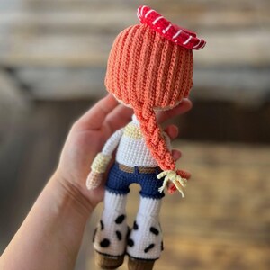 May include: A crocheted doll with orange hair, a red and white striped hat, a white shirt, blue jeans, and white boots with black spots.