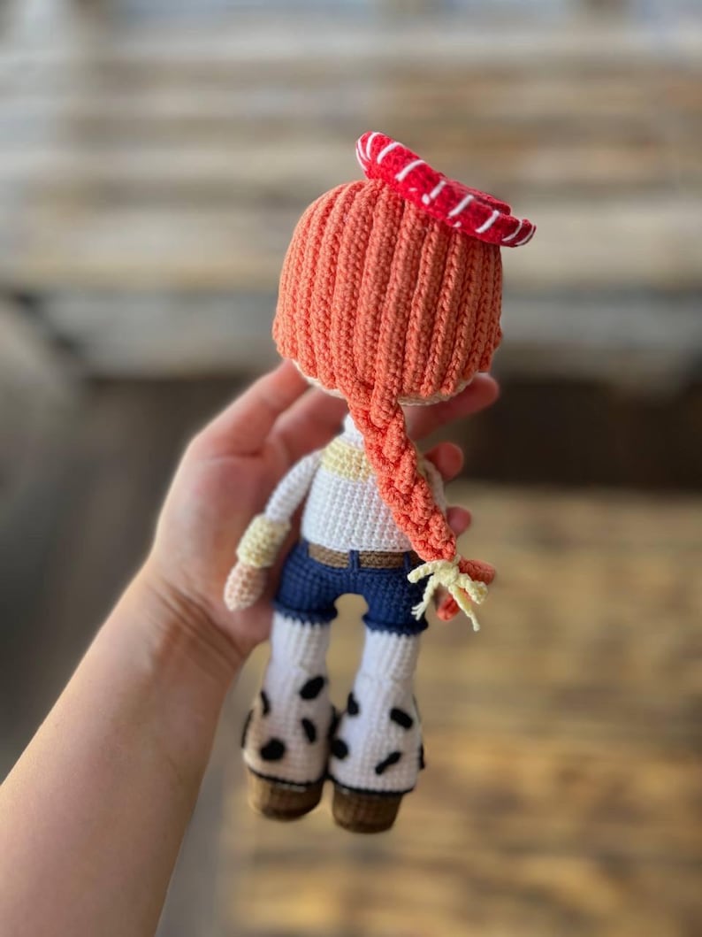 May include: A crocheted doll with orange hair, a red and white striped hat, a white shirt, blue jeans, and white boots with black spots.
