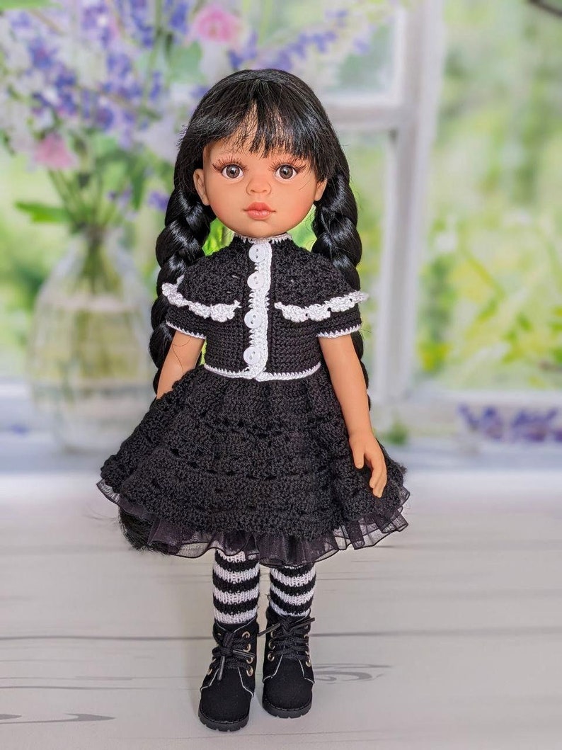 May include: A black and white crocheted dress with a white lace trim and black boots. The doll has black hair in braids and brown eyes.