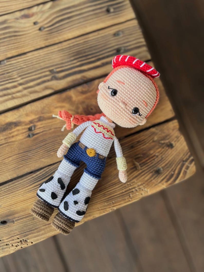 May include: A crocheted doll with red hair, a red and white hat, a white shirt with a yellow star, blue jeans, and white boots with black spots.