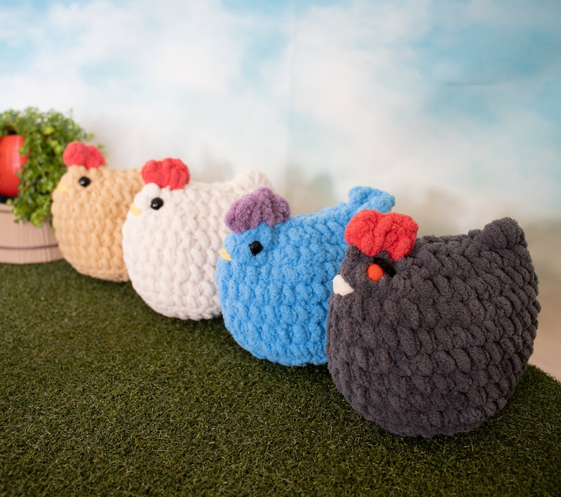 May include: Four crocheted chicken plushies in different colors: brown, white, blue, and gray. The plushies are arranged in a row on a green surface.