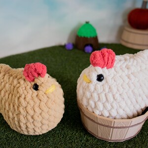 May include: Two crocheted plush chickens, one brown and one white, with red combs. The white chicken is sitting in a wooden bucket.