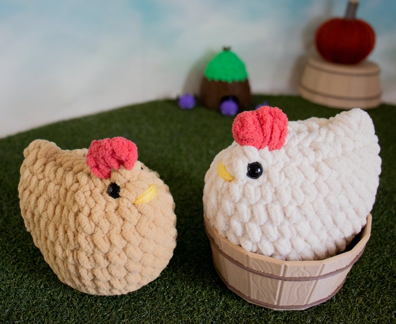 May include: Two crocheted plush chickens, one brown and one white, with red combs. The white chicken is sitting in a wooden bucket.