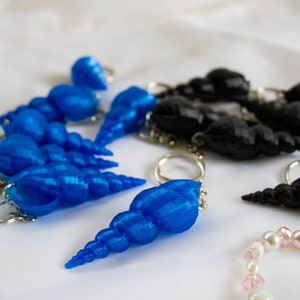 Op de afbeelding: Een set blauwe schelp sleutelhangers met zilveren ringen. De schelpen zijn in een rij gerangschikt, met de grootste schelp aan het einde van de rij. De schelpen zijn allemaal van verschillende grootte en vorm.