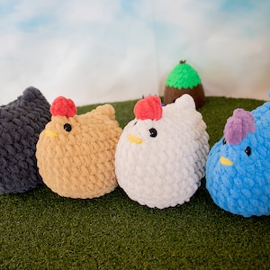May include: Four crocheted plush chickens in different colors: black, brown, white, and blue. The chickens are arranged in a row on a green surface.