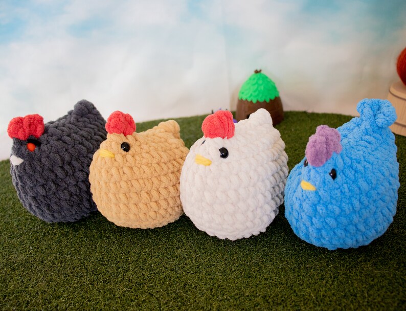 May include: Four crocheted plush chickens in different colors: black, brown, white, and blue. The chickens are arranged in a row on a green surface.