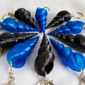 Op de afbeelding: Een set van tien sleutelhangers met een spiraalvormig schelpontwerp. Vijf van de sleutelhangers zijn blauw en vijf zijn zwart.