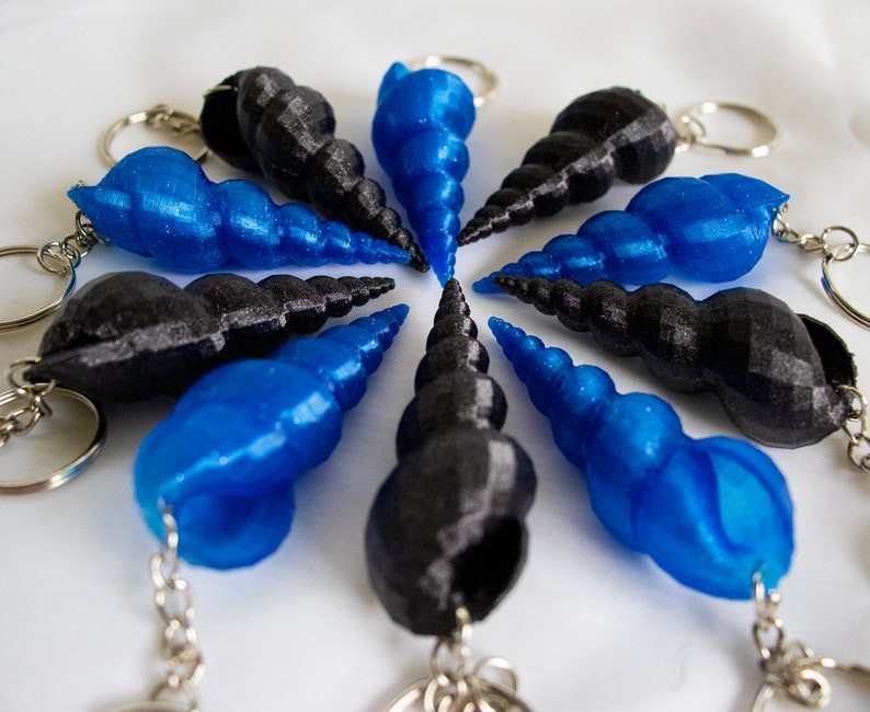 Op de afbeelding: Een set van tien sleutelhangers met een spiraalvormig schelpontwerp. Vijf van de sleutelhangers zijn blauw en vijf zijn zwart.