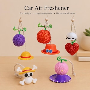 May include: A collection of car air fresheners featuring colourful designs. The image includes a purple sphere, a red fruit, a white hat with a heart, and a skull with a yellow hat. Text reads "Car Air Freshener" and "Fun designs • Long-lasting scent • Handmade with care."