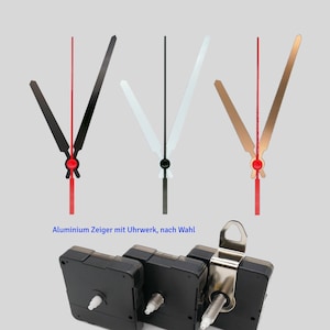 Op de afbeelding: Drie sets wijzers voor een klok in zwart, wit en goud met rode punten. De wijzers zijn gemaakt van aluminium en zijn bedoeld voor gebruik met een klokmechanisme. Het klokmechanisme is ook op de afbeelding te zien. Het mechanisme is zwart en heeft een zilveren metalen beugel.