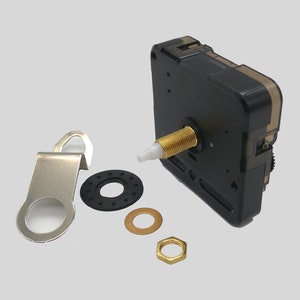 Op de afbeelding: Een zwart uurwerk met een goudkleurige schroefdraadas, een zilveren metalen hanger en diverse kleine hardware onderdelen. Inclusief een zwarte rubberen ring, een goudkleurige ring en een goudkleurige zeskantmoer.