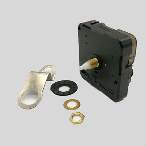 Könnte beinhalten: Uhrwerk-Kit mit einem schwarzen Kunststoff-Uhrwerk, einer Messingfarbenen Gewindewelle und verschiedenen Montageteilen. Enthält einen Metallbügel, eine Gummischeibe, eine Messingscheibe und eine Messing-Sechskantmutter.