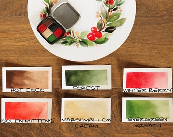 Può includere: Sei campioni di vernice ad acquerello su cartoncini bianchi con nomi scritti sotto ogni campione. I campioni sono: Hot Coco, Forest, Winter Berry, Woolen Mittens, Marshmallow Cream ed Evergreen Wreath.
