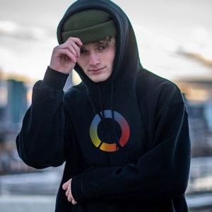 Peut inclure: Une personne portant un sweat-shirt à capuche noir avec un logo circulaire coloré et un bonnet vert.