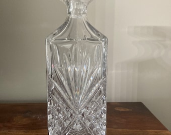 May include: A clear glass decanter with a square body and a faceted design. The decanter has a stopper with a square top.