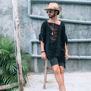 Puede incluir: Una persona con un top negro deshilachado con flecos, un sombrero marr&oacute;n, gafas de sol y varios collares. La persona est&aacute; de pie en una plataforma de hormig&oacute;n con un taburete de madera.