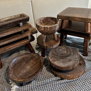 Puede incluir: Una colección de bandejas de servir, cuencos y taburetes de madera en varios tamaños y formas. Los artículos están hechos de madera marrón oscura con un acabado rústico.