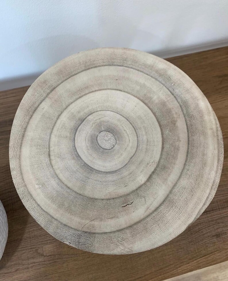 May include: A round, light-colored wooden table top with concentric rings, resembling tree rings. The table top is made of natural wood and has a rustic, organic aesthetic. The diameter is approximately 24 inches.