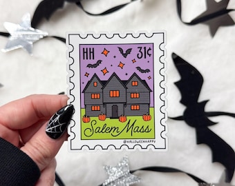 Puede incluir: Una pegatina con forma de sello postal con una casa negra con ventanas naranjas y calabazas. El texto "Salem Mass" está escrito en verde. El sello tiene un fondo morado con murciélagos y estrellas.