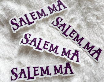 Puede incluir: Cuatro pegatinas blancas con el texto "Salem, MA" en letras moradas. Las pegatinas están sobre una superficie blanca y peluda.