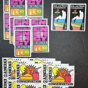 May include: A collection of vintage United States postage stamps featuring the themes of energy conservation and soil and water conservation. The stamps feature various designs, including a sun, a light bulb, and a hand holding a plant.