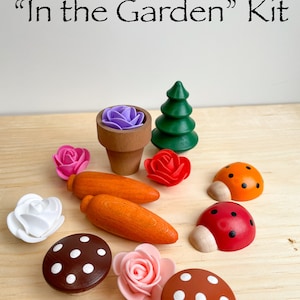 Puede incluir: Un juego de madera con el t&iacute;tulo "In the Garden" Kit. El juego incluye un peque&ntilde;o &aacute;rbol de madera, dos setas con lunares blancos, dos mariquitas, una zanahoria, una maceta con una flor morada y tres flores rosas.