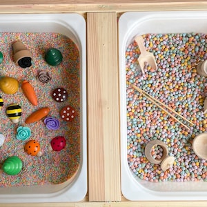 Puede incluir: Dos bandejas blancas llenas de materiales sensoriales coloridos. La bandeja de la izquierda tiene una variedad de peque&ntilde;os juguetes de madera, incluyendo flores, mariquitas, abejas y zanahorias. La bandeja de la derecha tiene una pala, un palo de madera y un peque&ntilde;o cuenco de madera.