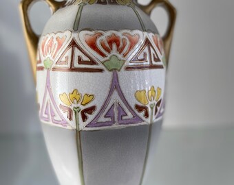 May include: A white ceramic vase with gold accents and a geometric floral design in shades of orange, yellow, green, purple, and brown. The vase has two handles and a rounded body.