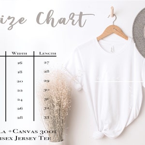Pu&ograve; includere: Una maglietta unisex bianca in jersey appesa a una gruccia di legno, accanto a un cappello grigio. Una tabella delle taglie mostra le misure in cm per le taglie XS-3XL. Il testo recita "Size Chart" e "BELLA + CANVAS 3001 UNISEX JERSEY TEE."