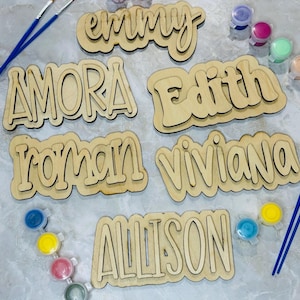 以下が含まれることがあります： 「emmy」、「AMORA」、「Edith」、「roman」、「viviana」、「ALLISON」という名前のウッドカットアウトと、絵の具の壺と筆。 これらは、自分で名前を塗るDIYサインです。
