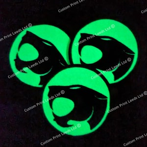 May include: Three glowing green circular coasters with a black panther silhouette. The coasters are arranged in a triangular pattern against a dark background. The text "Custom Print Leeds Ltd" is printed around the edge of each coaster.