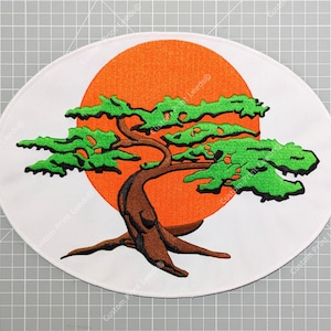 Può includere: Toppa ovale con un disegno di bonsai. L'albero ha foglie verdi e un tronco marrone, su uno sfondo di sole arancione su sfondo bianco. Il disegno è ricamato.