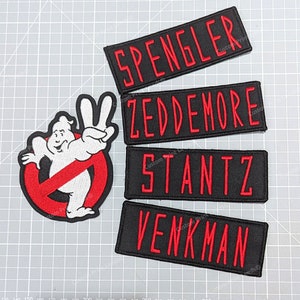 May include: Four black embroidered patches with red lettering. The patches read "Spengler", "Zeddmore", "Stantz", and "Venkman". A red and white patch with a ghost wearing a no ghost sign is also included.
